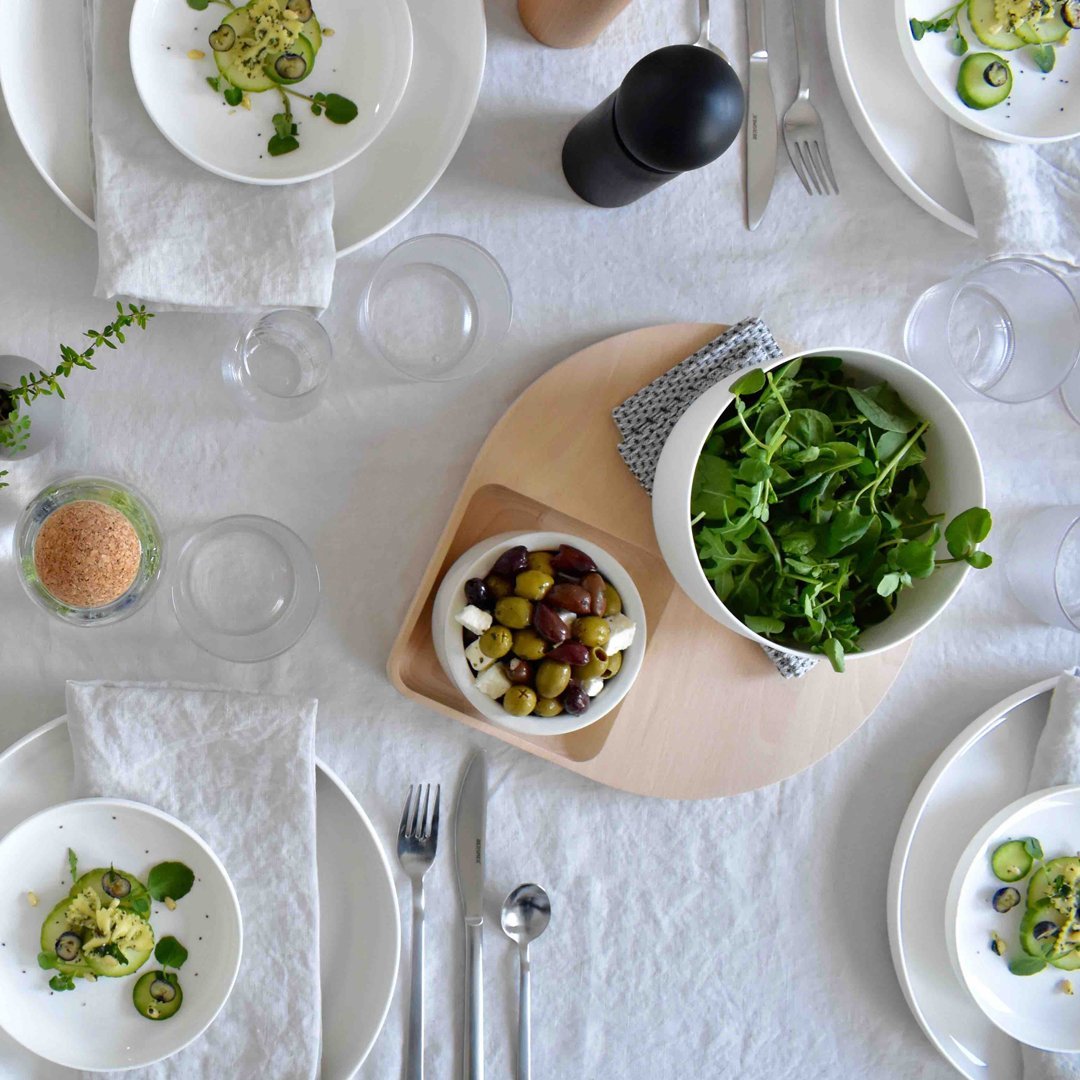 "Elegant white dinnerware set arranged on a light tablecloth with green salad and colorful olives in a bowl."