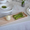 Light wood serving tray with ribbed pattern, showcasing green asparagus and creamy sauce against a neutral table setting.