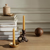 "Rustic brown candles in unique holders, golden accents, and neutral tones against stacked books on a wooden surface."