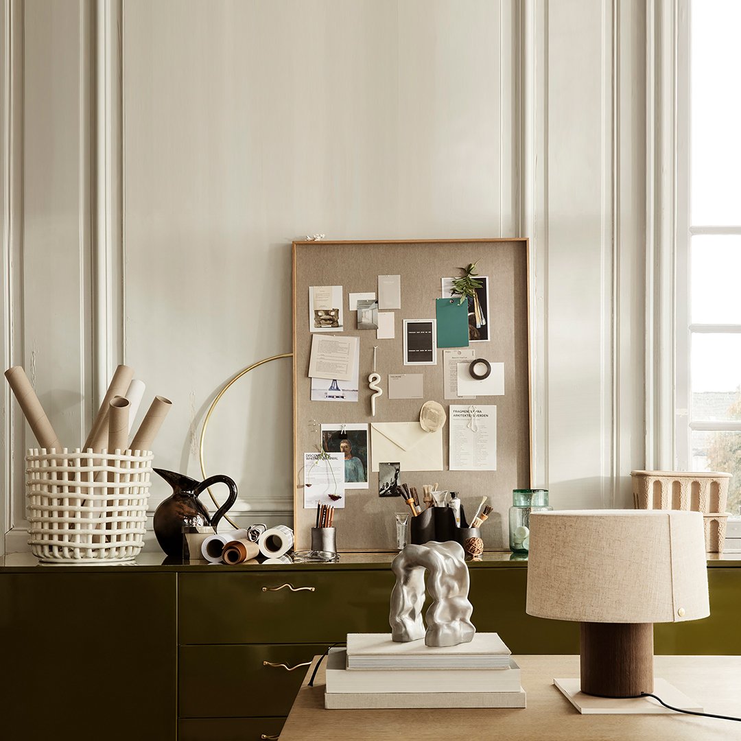 "Muted earth tones with a mix of textures; features a green cabinet, soft beige lamp, and a natural woven basket."