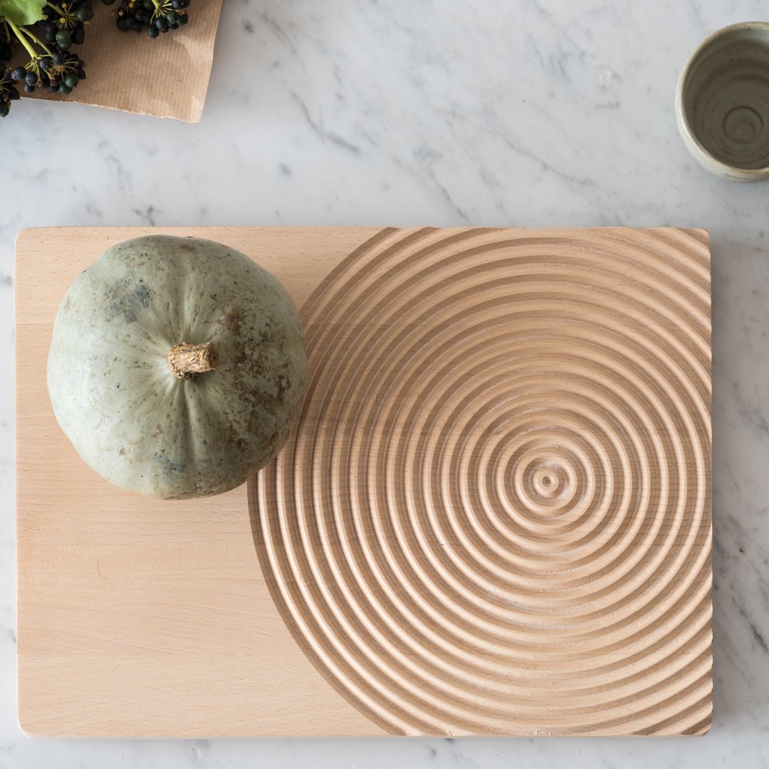 Natural wood cutting board with a spiral pattern, featuring a green pumpkin for decorative contrast.