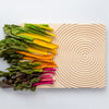 Colorful Swiss chard in yellow, orange, and pink, arranged on a textured wooden cutting board with concentric circles.
