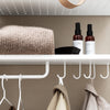 Soft beige sweater, black hair comb, and brown spray bottles on a white shelf against a neutral wall. Modern and minimalist.